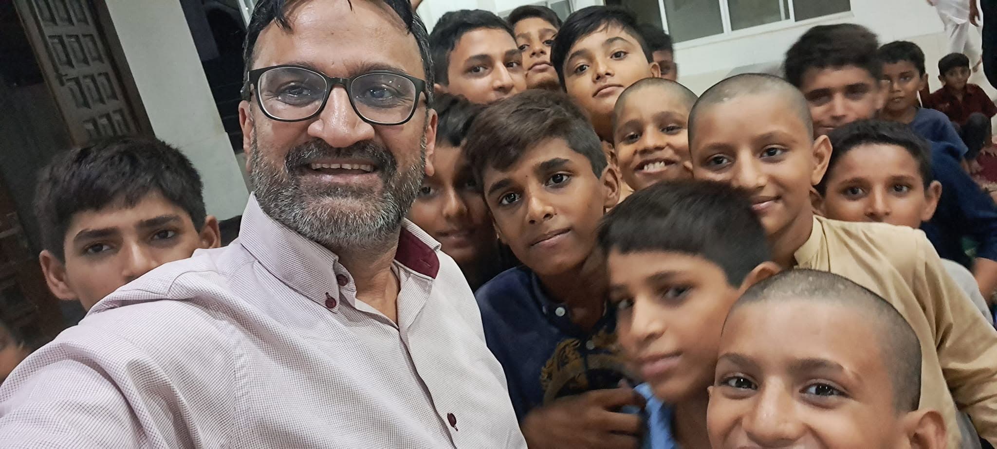 A man from the foundation surrounded by a crowd of smiling boys, leaning in together for a photograph in a hallway at an orphanage.